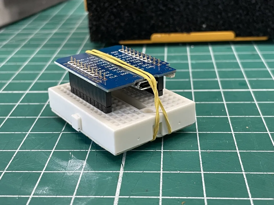 Small breadboard with a mounted breakout board, secured by a rubber band on a green cutting mat.